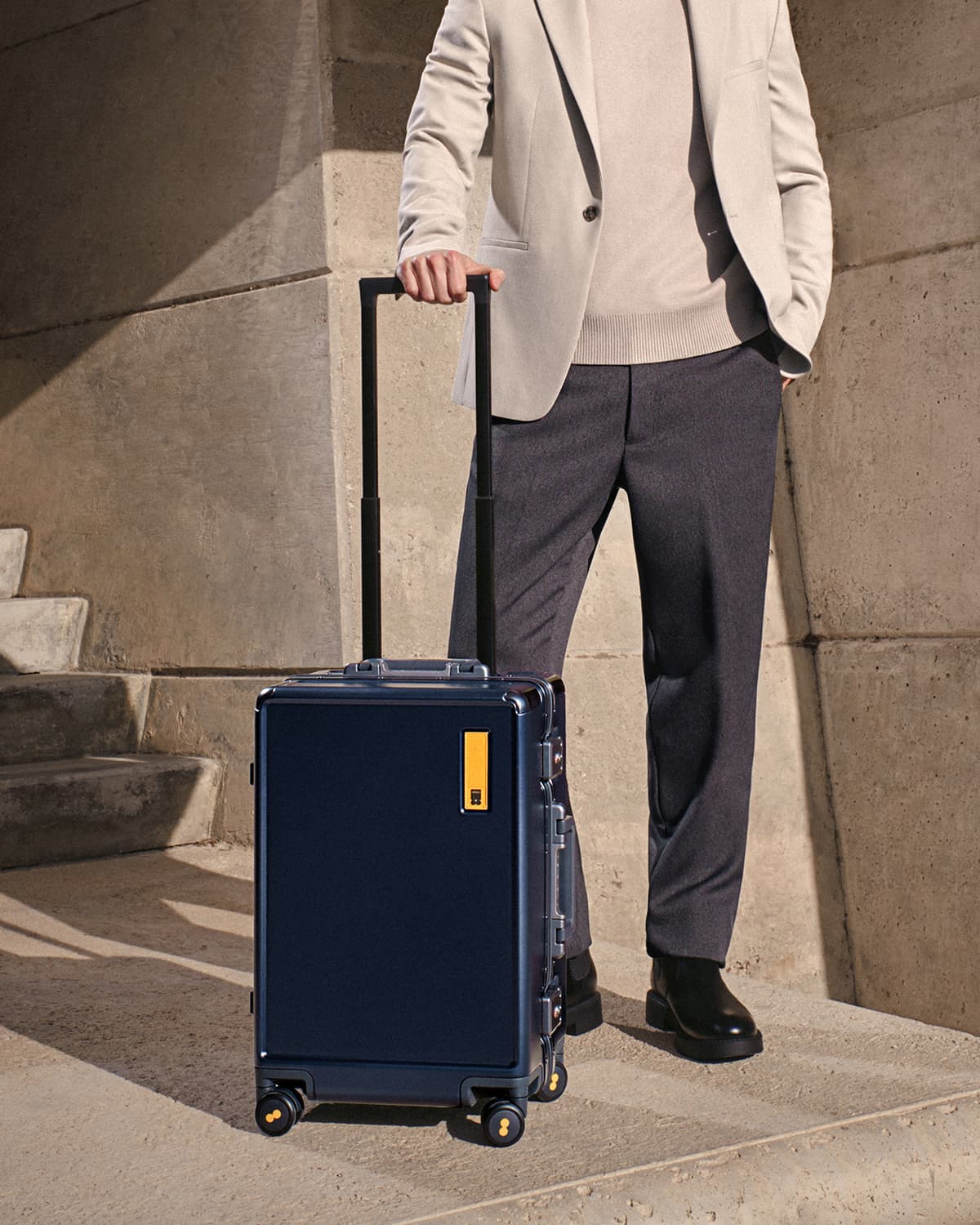 Man standing on stone steps pulling Hegent Carry On 20" Navy suitcase